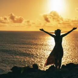 mujer feliz brazos abiertos atardecer en el mar de espaldas