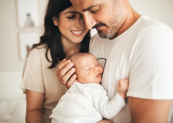 Un hombre cogiendo a un bebé mientras una mujer les mira sonriendo