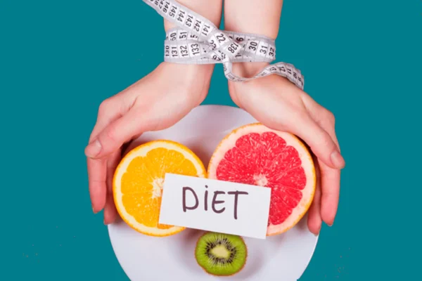 manos atadas con cinta metrica sujetando un plato con tres frutas partidas y un letrero encima que pone en negro y mayusculas diet