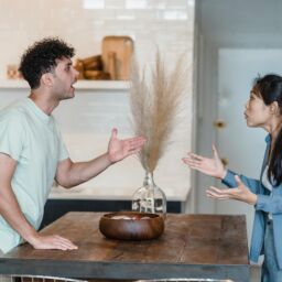 hombre y mujer hablando , gesticulando con las manos, separados por una mesa en medio.
