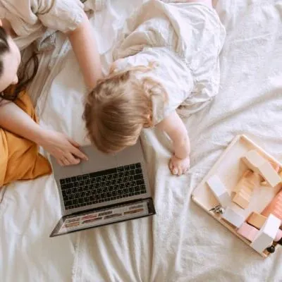 mujer con bebe en la cama con el ordenador y con una bandeja con objetos