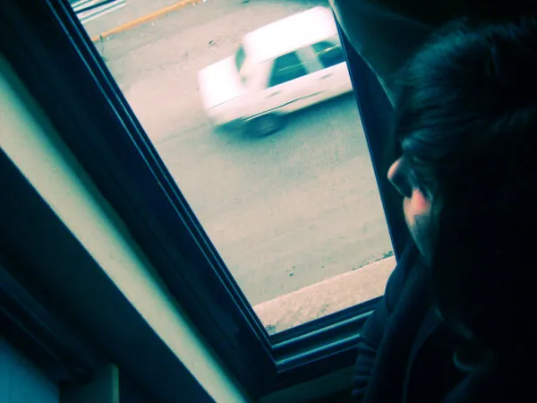 PERSONA MIRANDO POR VENTAN DE CASA FOTO EN NEGATIVO EN VENTANA SE VE UN COCHE BLANCO CIRCULANDO