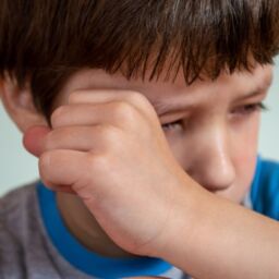 niño llorando frotandose el ojo con el puño de la mano con camiseta azul y gris