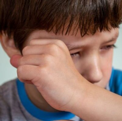 niño llorando frotandose el ojo con el puño de la mano con camiseta azul y gris