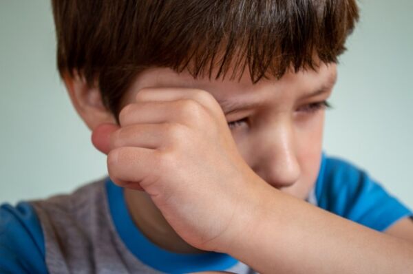 niño llorando frotandose el ojo con el puño de la mano con camiseta azul y gris